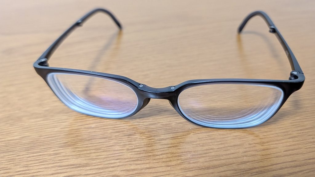 机の上に置いたJINS Halfのメガネ。黒いマットな樹脂フレームで、鼻の部分に折りたたみの継ぎ目がある新しく買ったJINS Half